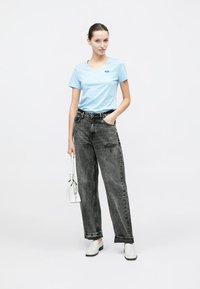 Φωτεινό γαλάζιο t-shirt με V λαιμόκοψη, μαύρο τζιν με ψηλή μέση και φαρδιά γραμμή με διακριτικό φθαρμένο μοτίβο, γκρι παπούτσια τύπου slip-on και λευκή τσάντα χειρός.