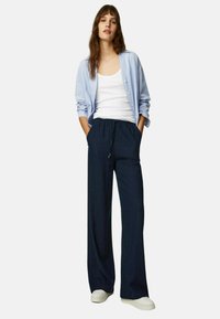 Losse marineblauwe broek met een tailleband met trekkoord, gecombineerd met een lichtblauw knoopshirt over een witte tanktop. Gladde stofstructuur.