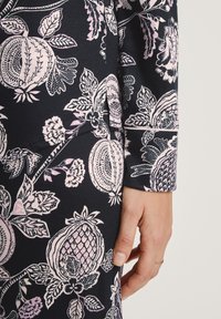 Details van een bloemenjurk met een marineblauwe stof met roze en witte botanische patronen, benadrukt door een slanke, fitted mouw en manchet.