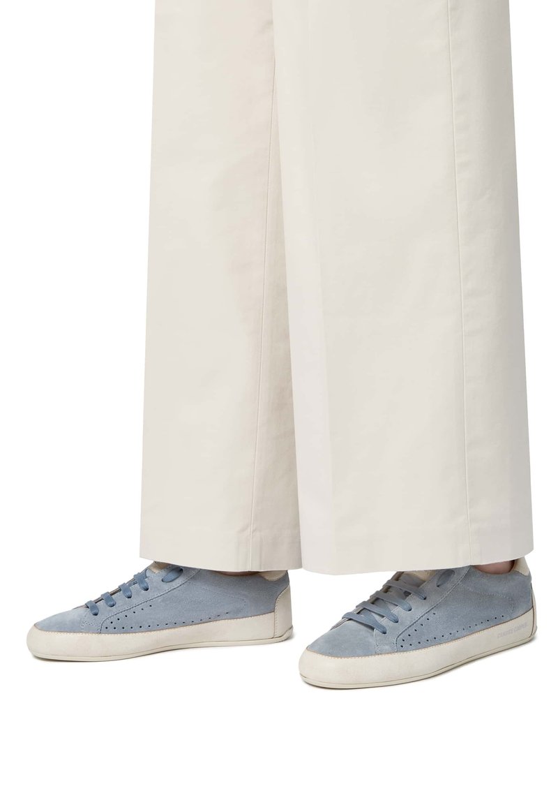 Sneakers blu in suede con lati perforati e suola in gomma bianca. I lacci abbinano il colore della scarpa. Indossati con pantaloni larghi di colore chiaro.
