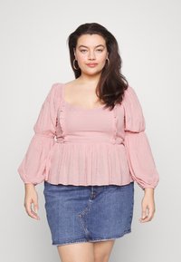 Blusa rosa clara com mangas balão, costuras franzidas e textura de bolinhas, combinada com uma saia mini de ganga. Tecido suave com detalhes franzidos.