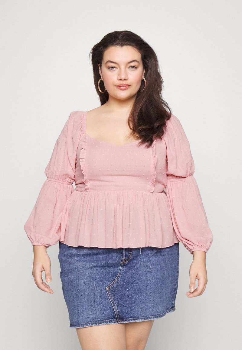 Blusa rosa clara com mangas balão, costuras franzidas e textura de bolinhas, combinada com uma saia mini de ganga. Tecido suave com detalhes franzidos.