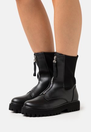 Stivaletti alla caviglia neri con tomaia in pelle e pannelli laterali elastici. Presentano zip argentate, suola carrarmato spessa e dettagli testurizzati.