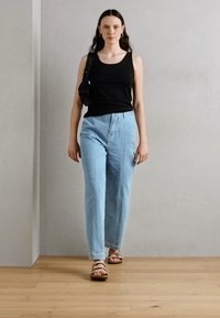 Black tank top, light blue high-waisted jeans, brown strappy sandals, styled with a black shoulder bag, against a neutral background.