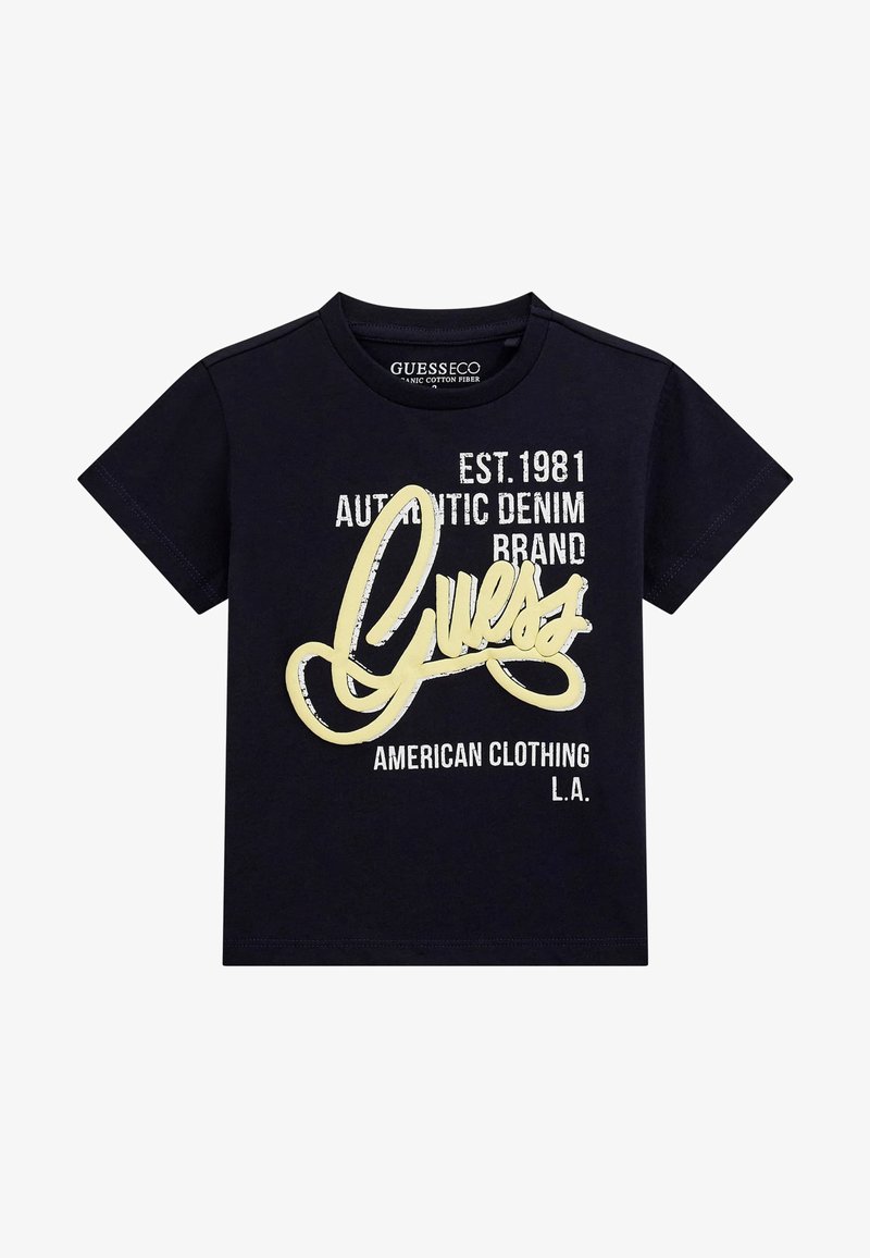 T-shirt in cotone blu navy con grande logo giallo "Guess" con testo stilizzato; presenta testo bianco con dettagli del marchio. Maniche corte.