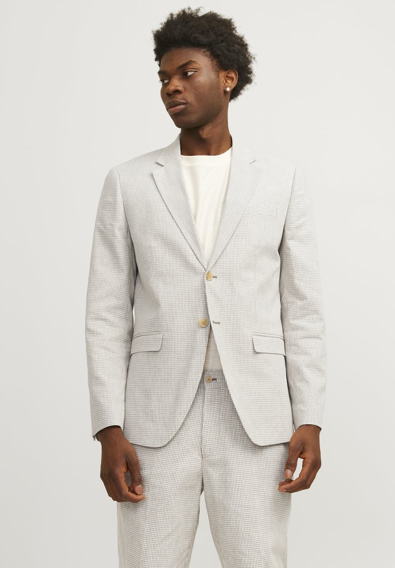 Blazer de patrón gris claro con pantalones a juego, que cuenta con un cierre de dos botones, solapas con muesca y bolsillos laterales. Textura de tela suave.