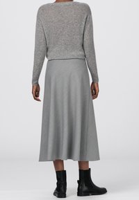 Harmaa mohairsekoite neule pitkähihaisilla hihoilla, yhdistettynä harmaaseen nilkkapituiseen hameeseen, jossa on hienovarainen herringbone-kuvio ja mustat nilkkurit.