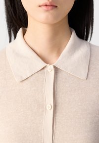 Beige collared genser med myk tekstur, knappelukking og et subtilt strikkemønster. Kragen er strukturert og har et klassisk design.