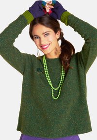 Green wool sweater with a round neckline and long sleeves. Worn with green bead necklaces and colorful fingerless gloves.