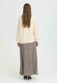 Pulover crem cu mâneci lungi și o fustă lungă, cu un model cu linii negre ondulate pe un fundal bej. Tocuri negre.