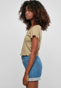 Haut à manches courtes khaki avec des bords effilochés, associé à un short en denim taille haute, avec un revers à l'ourlet.