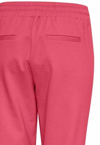 Pantaloni della tuta rosa realizzati in tessuto morbido, con una cintura elastica e due tasche posteriori con aperture rettangolari.