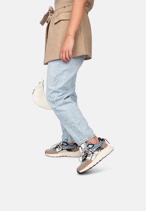 Sneakers con un design beige e grigio, caratterizzati da materiali in mesh e tessuto, suole spesse, accenti blu e lacci a fantasia. Jeans chiari e una maglietta beige.
