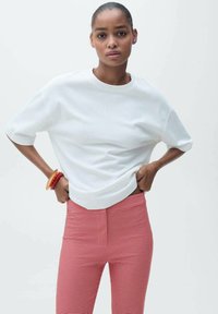Weißes T-Shirt mit kurzen Ärmeln und Rundhalsausschnitt, kombiniert mit rot-weiß karierten, figurbetonten Hosen. Glatter Stoff mit entspannter Passform.
