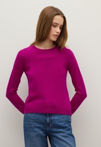 Fuchsia Pullover mit langen Ärmeln, Rundhalsausschnitt und geripptem Saum. Aus weichem Wollgemisch. Kombiniert mit lässigen blauen Jeans.