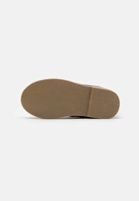 Schuhsohle nach oben mit einer strukturierten braunen Gummibasis und einer geriffelten Linie, die die Zehen- und Fersenbereiche trennt.
