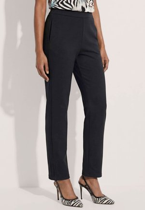 Frau trägt schwarze Slim-Fit-Hosen kombiniert mit zebra-print High-Heel-Slingback-Schuhen und einem gemusterten Top.