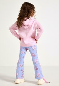 Ljusrosa hoodie med en framficka, matchad med ljusblå utsvängda byxor med ett mönster av rosa rosor. Avslappnade sneakers fulländar outfiten.