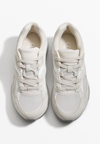 Világosszürke sportcipők, hálós és velúr anyagból, kerek orral, fűzővel és logóval a nyelven. Enyhén párnázott bokarész a kényelem érdekében.