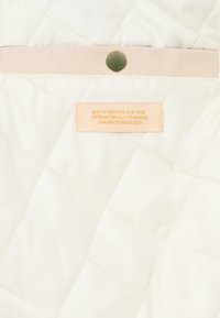 Quilttet creme stof med en subtil glans, der har en lys beige læderlap og en prægning af label i blød orange, der angiver brandinformation.