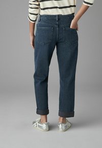 Jean en denim bleu foncé à coupe décontractée, avec des poignets retroussés, deux poches arrière et une ceinture classique.