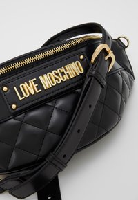 Černá prošívaná taška z umělé kůže se zlatými kovovými detaily, která má vpředu znak s nápisem "LOVE MOSCHINO" a nastavitelný popruh.