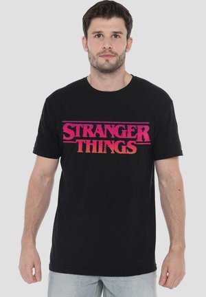 Black cotton t-shirt featuring "STRANGER THINGS" logo in gradient pink and orange text across the chest. Crew neck and short sleeves.