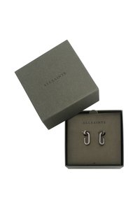 Boucles d'oreilles en métal argenté au design de créole unique, présentées dans une boîte vert foncé avec le nom de la marque "ALLSAINTS" embouti sur le couvercle.