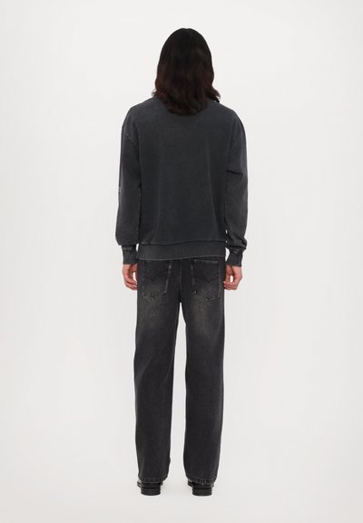 Sweatshirt oversize gris foncé avec des poignets et un ourlet côtelés, associé à un jean noir ample avec poches arrière et texture décolorée.