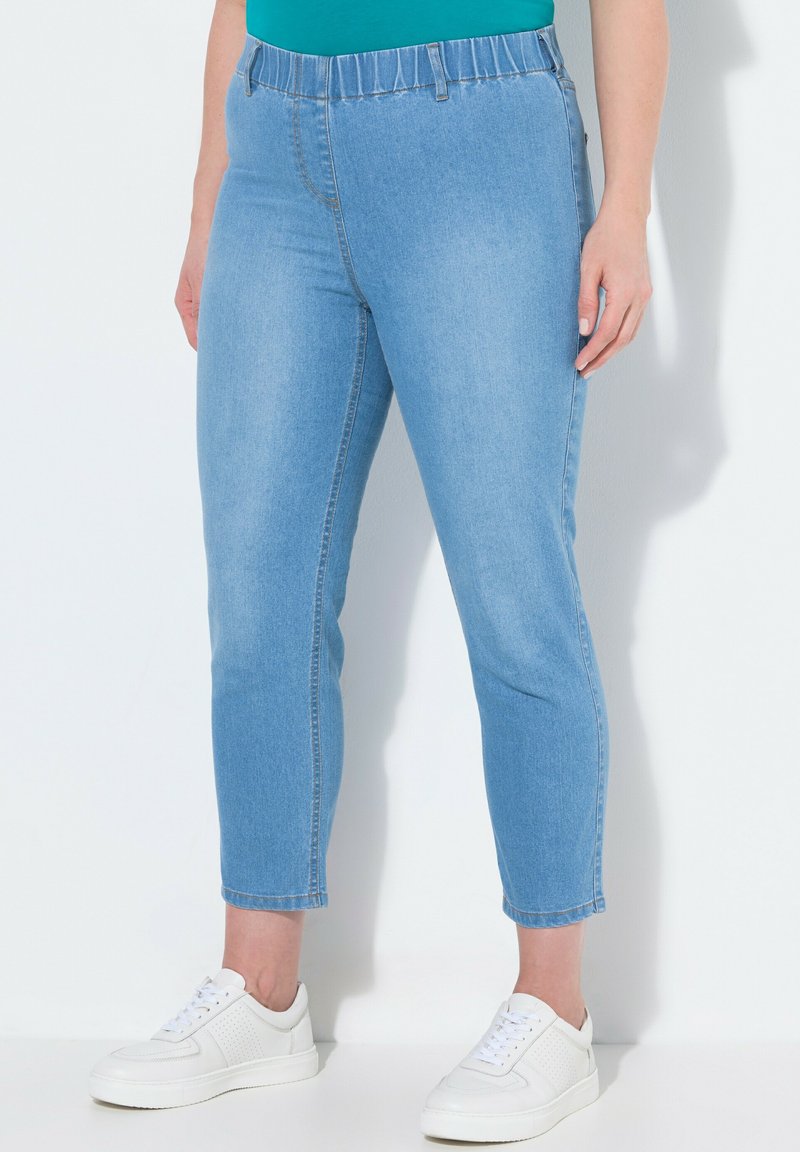 Světle modré džínové cropped kalhoty s elastickým pasem a zúženými nohavicemi, v kombinaci s bílými teniskami. Hladká, lehce elastická tkanina.