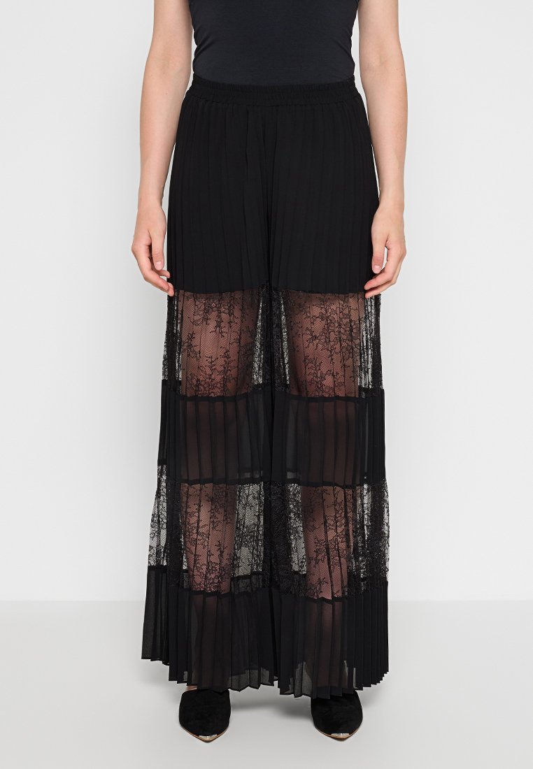 Pantalons plissés noirs avec des sections en dentelle transparente. Dotés d'une taille élastique et d'un design superposé, créant une apparence fluide et texturée.