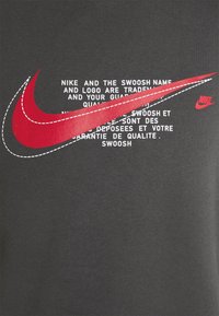Sweatshirt noir avec un grand logo Swoosh rouge de Nike accompagné de texte blanc. Texture lisse avec des détails de couture autour du Swoosh.
