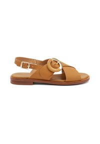Sandalini slingback in pelle tan con un accento circolare dorato, fasce incrociate e suola piatta in legno. Chiusura con fibbia regolabile.