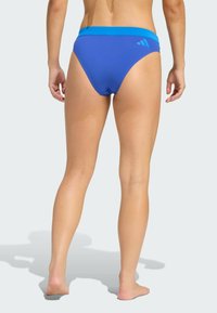 Modré plavky s bikiny spodnou časťou s kontrastným svetlomodrým pásom, s elegantným dizajnom a minimálnymi logovými akcentmi. Hladká textúra látky.