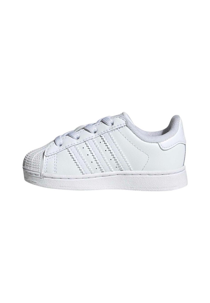 White synthetic leather sneaker with a textured toe cap, lacing, three stripes, and a flat rubber sole. Classic low-top design, minimalist style.