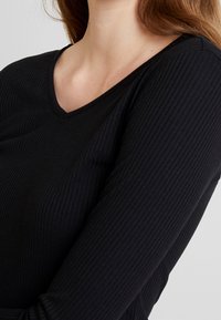 Musta, ribbed pitkähihainen paita, jossa on v-pääntie. Kankaan pinta on sileä ja malli istuva. Ei näkyviä kuvioita tai koristeita.