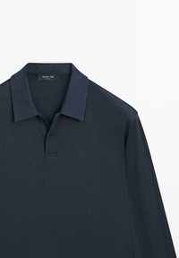 Polo bleu marine foncé en coton. Doté d'un col classique, d'une patte de boutonnage et de manches courtes avec une texture lisse. Étiquette visible.