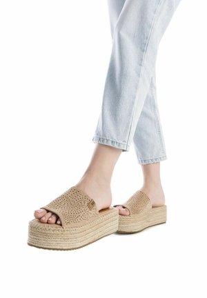Sandalias de cuña beige con diseño perforado, plantilla similar a yute y suela plana, combinadas con unos vaqueros cropped de color azul claro.