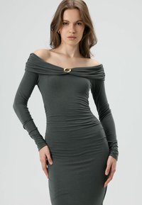 Robe à manches longues et épaules dénudées en tissu gris foncé avec fronces et détail de fermoir doré au niveau de l'encolure. Texture lisse.