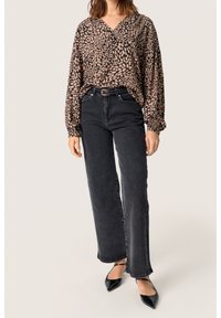 Blusa marrone a motivo con maniche voluminose, abbinata a jeans neri a vita alta e gamba dritta e tacchi a punta neri.