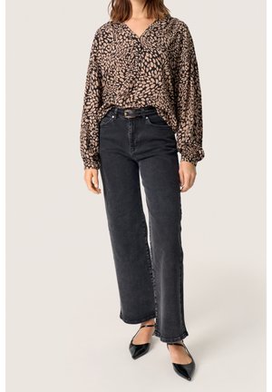 Braune Bluse mit Muster und voluminösen Ärmeln, kombiniert mit hochtaillierten schwarzen, geraden Jeans und schwarzen spitzen Pumps.