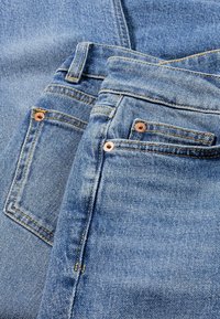 Jeans de mezclilla en azul claro con costuras doradas en contraste. Cuenta con bolsillos con remaches de cobre y un acabado suave y texturizado.