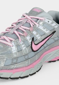 Γκρι και ροζ αθλητικό παπούτσι Nike με επάνω μέρος από δίχτυ, ροζ κορδόνια και ροζ λογότυπο Swoosh με μαύρο περίγραμμα στο πλάι.