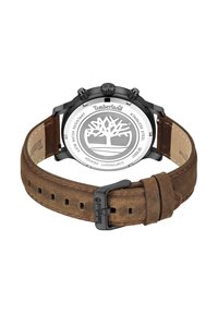 Reloj con correa de cuero marrón y respaldo de acero inoxidable, bisel negro y logo de Timberland grabado. Presenta un diseño de árbol en la caja.