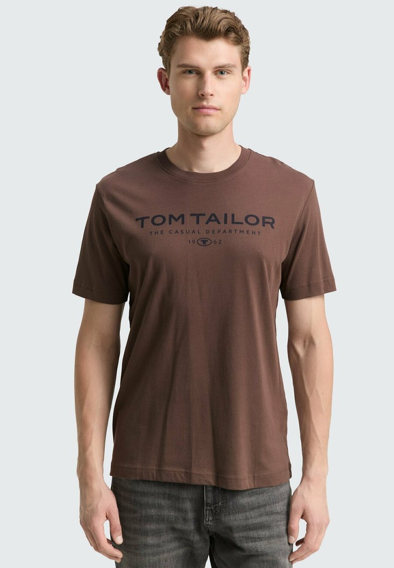 Bruine katoenen t-shirt met korte mouwen en een ronde hals. Voorzien van een donkerblauwe bedrukte logo-tekst over de borst.