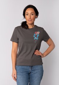 Graues T-Shirt mit kurzen Ärmeln, das ein farbenfrohes Grafikdesign eines Blitzes und Rollschuhe im linken Brustbereich zeigt, aus einem Baumwollmischgewebe hergestellt.
