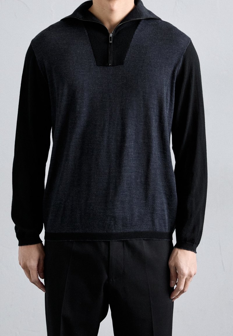Pull-over foncé avec un col zippé. Présente une combinaison de couleurs gris foncé et noir, une silhouette structurée et des poignets côtelés. Texture solide.