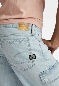  Lichtblauwe denim cargo broek met zichtbare stiksels, een leren G-Star label op de tailleband en een zwart stoffen merkteken op de zijzak.