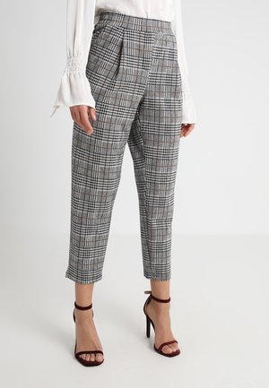Woman wearing gray and black checkered cropped trousers paired with burgundy high-heeled sandals and a white blouse with flared cuffs.
