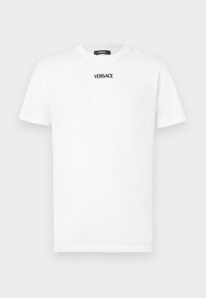 Valkoinen puuvillainen T-paita, jossa on lyhyet hihat, pyöreä kaula-aukko ja musta "VERSACE"-logo rintakehässä. Klassinen istuvuus ja sileä pinta.
